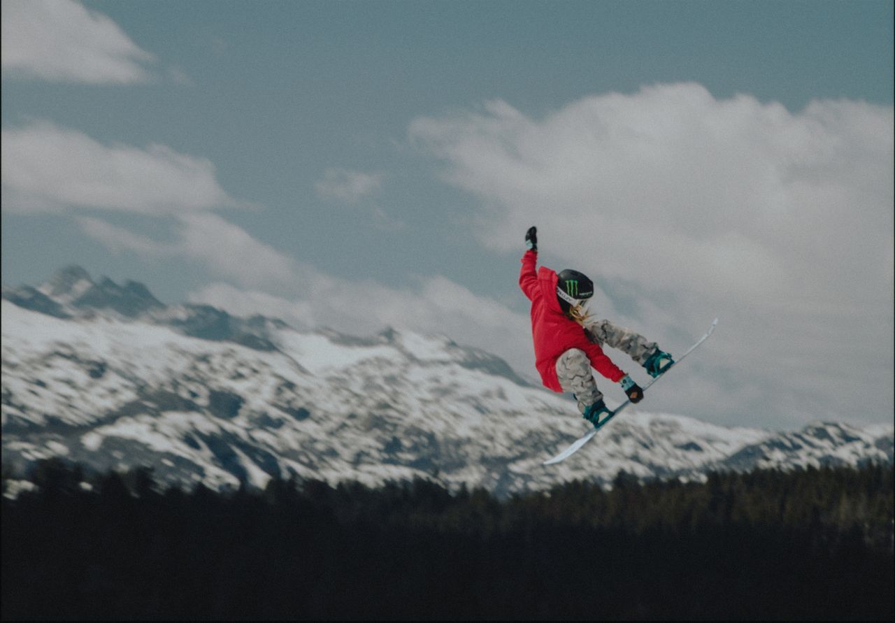 Snowboarder in red jacket mid-air against snowy mountains