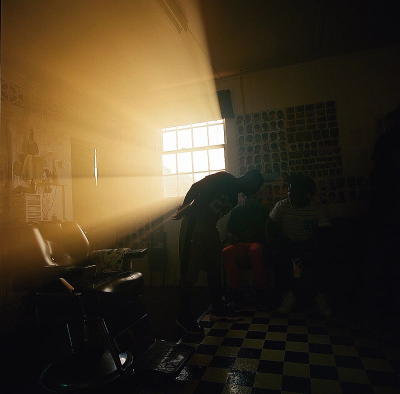 Backlit figures in a barbershop with dramatic golden hour sunlight and checkered floor.