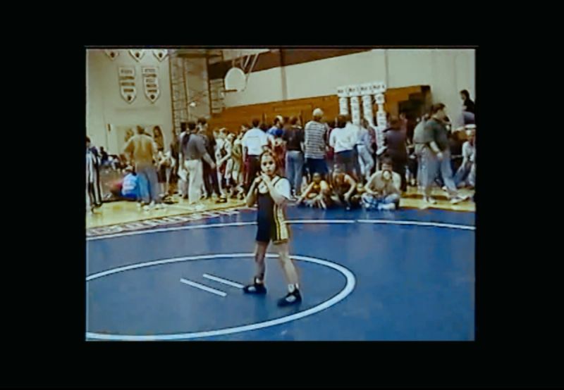 Olympic wrestler Helen Maroulis stands on a blue wrestling mat in a gymnasium during the EastBay ConqHer project.
