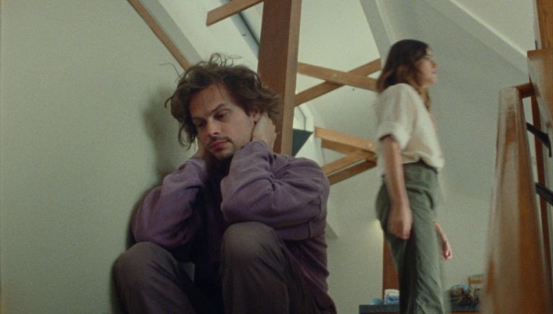Will Mayer sits on stairs in contemplation, woman stands nearby in Future Islands Moonlight.