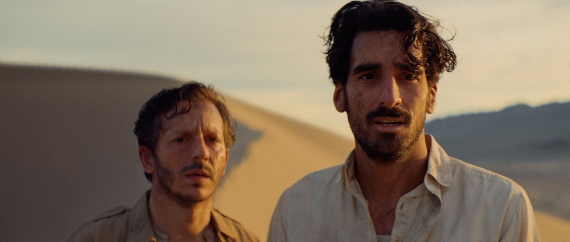 Two men stand in desert dunes under warm golden light, cinematic film photography.