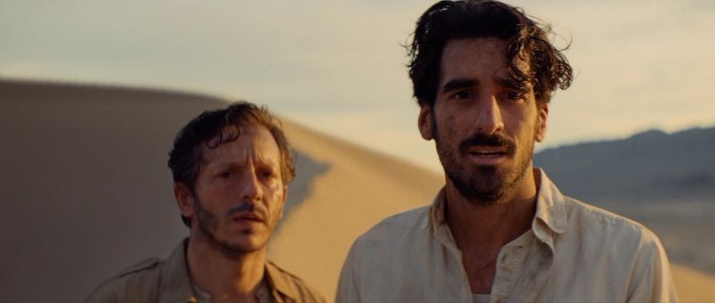 Two men stand in desert dunes under warm golden light, cinematic film photography.