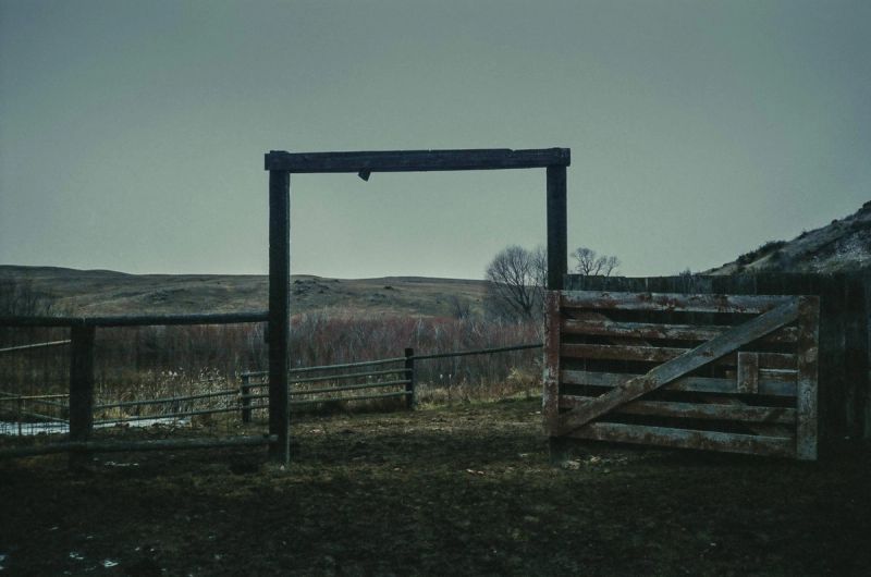 Weathered wooden gate and fence frame in open field under overcast sky