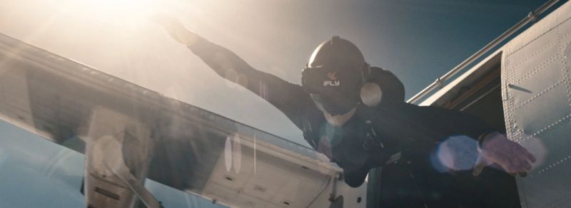 Skydiver exiting aircraft with arms outstretched against bright sun, iFly VR project still.