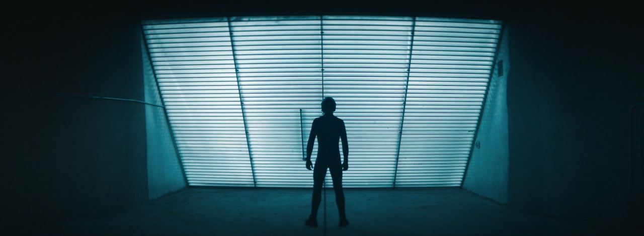 Silhouette of a person standing in front of a large illuminated window with horizontal slats.