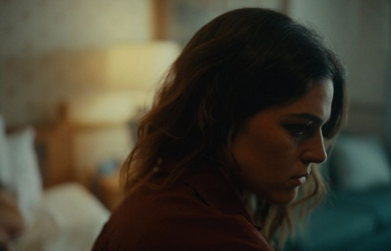Close-up of woman in dimly lit room, looking down with somber expression