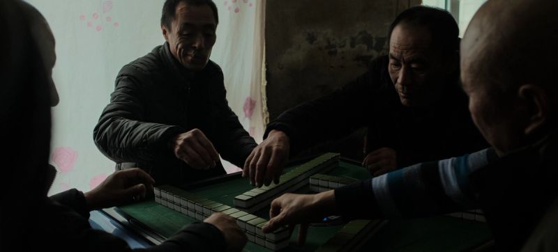 Cinematic still of men playing mahjong tiles at a table in dim light, Jilin China.
