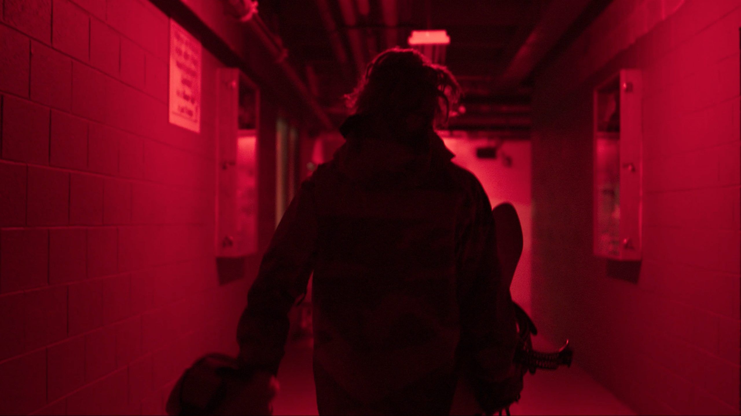 Cinematography of a snowboarder walking through a red-lit hallway carrying equipment.