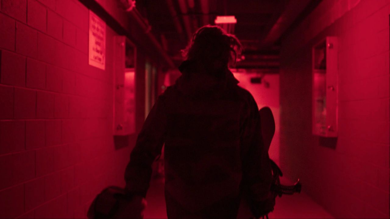 Cinematography of a snowboarder walking through a red-lit hallway carrying equipment.