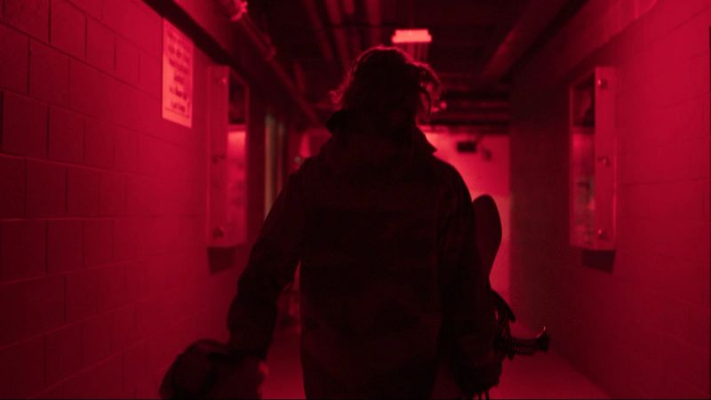 Cinematography of a snowboarder walking through a red-lit hallway carrying equipment.