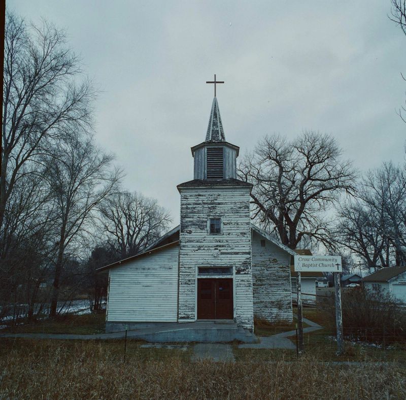 Weathered white church tower with cross stands near Crow Community Baptist Church sign.