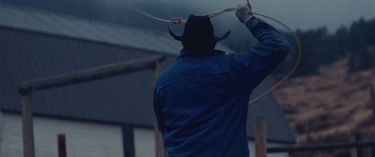 Cinematographer in cowboy hat swinging lasso near barn on Montana ranch
