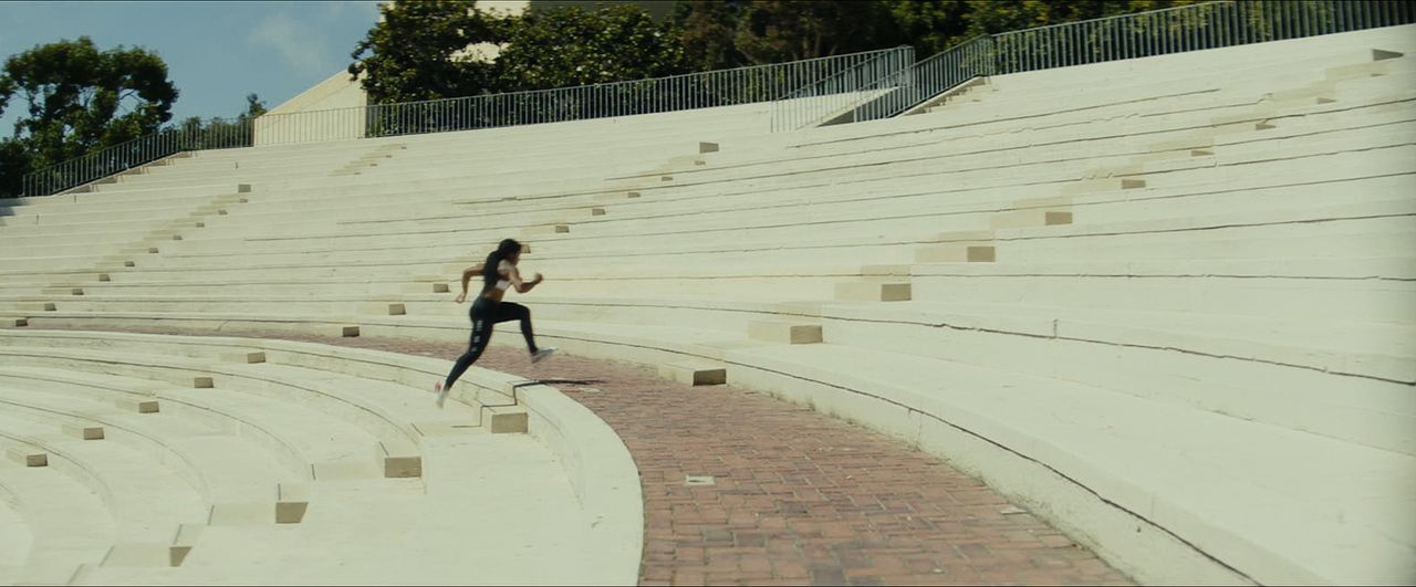 Woman running up white concrete stadium bleachers in an outdoor amphitheater.