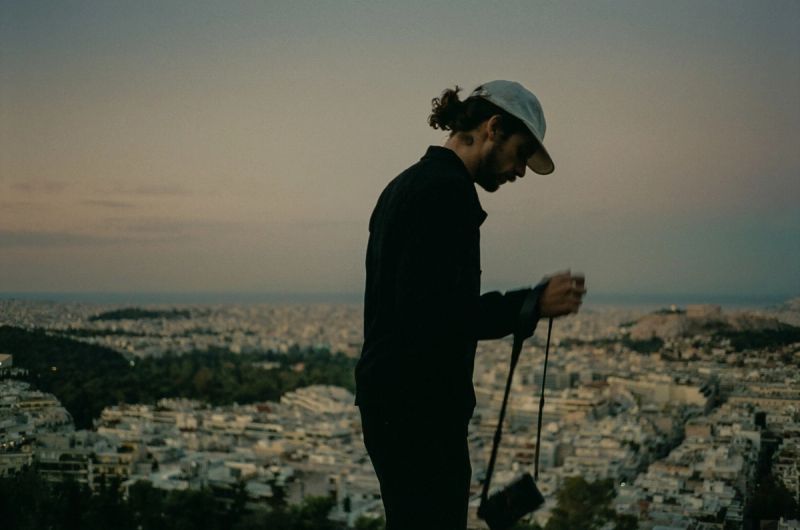 Cinematographer holding a camera while overlooking a sprawling cityscape at dusk.
