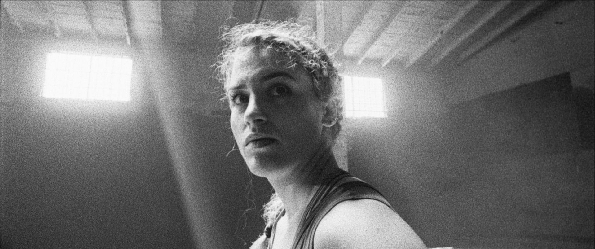 Black and white film photo of Olympic wrestler Helen Maroulis looking back in a gym with bright windows.