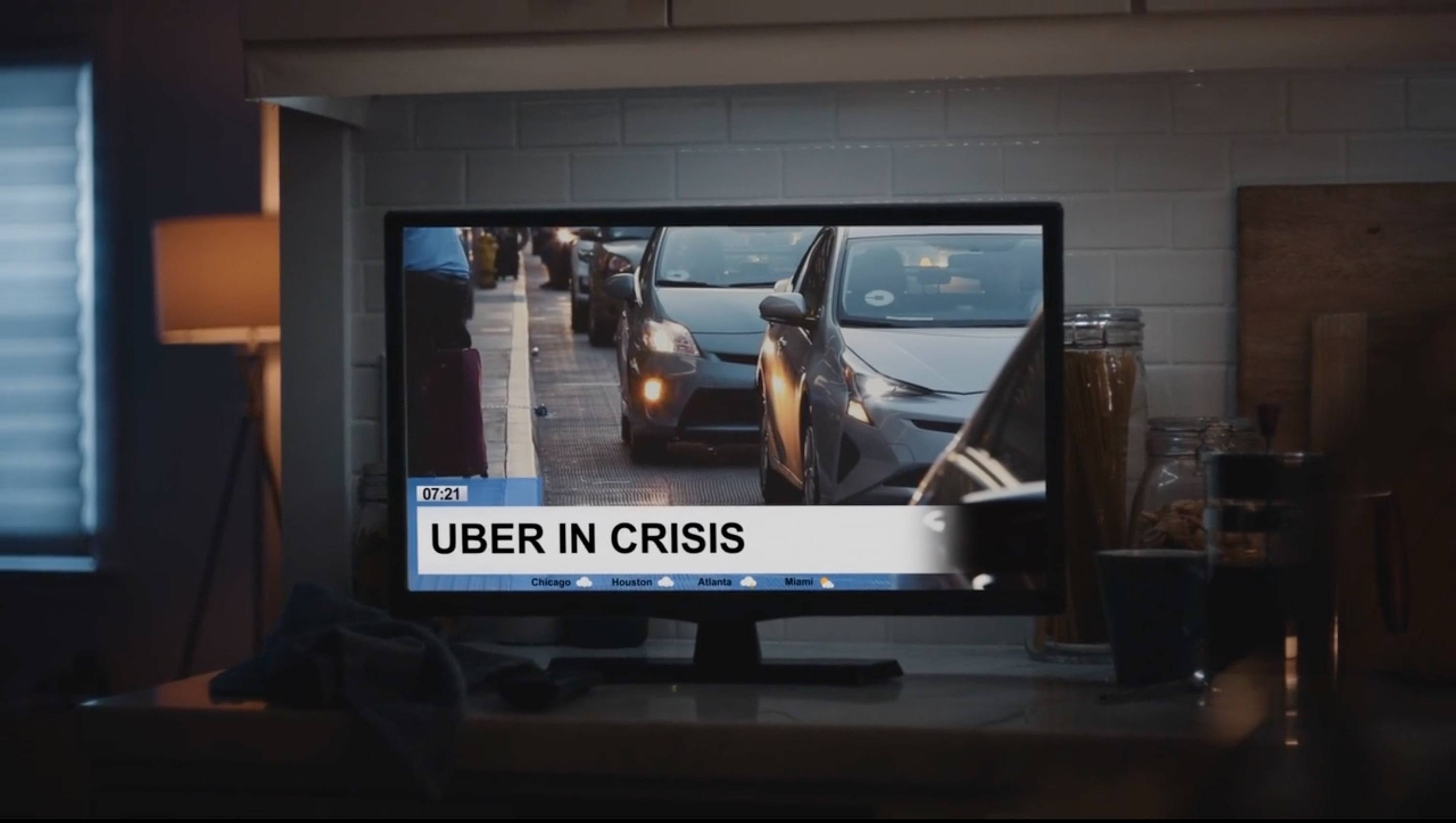 A television screen displays a news report with the headline 'UBER IN CRISIS' over footage of cars.