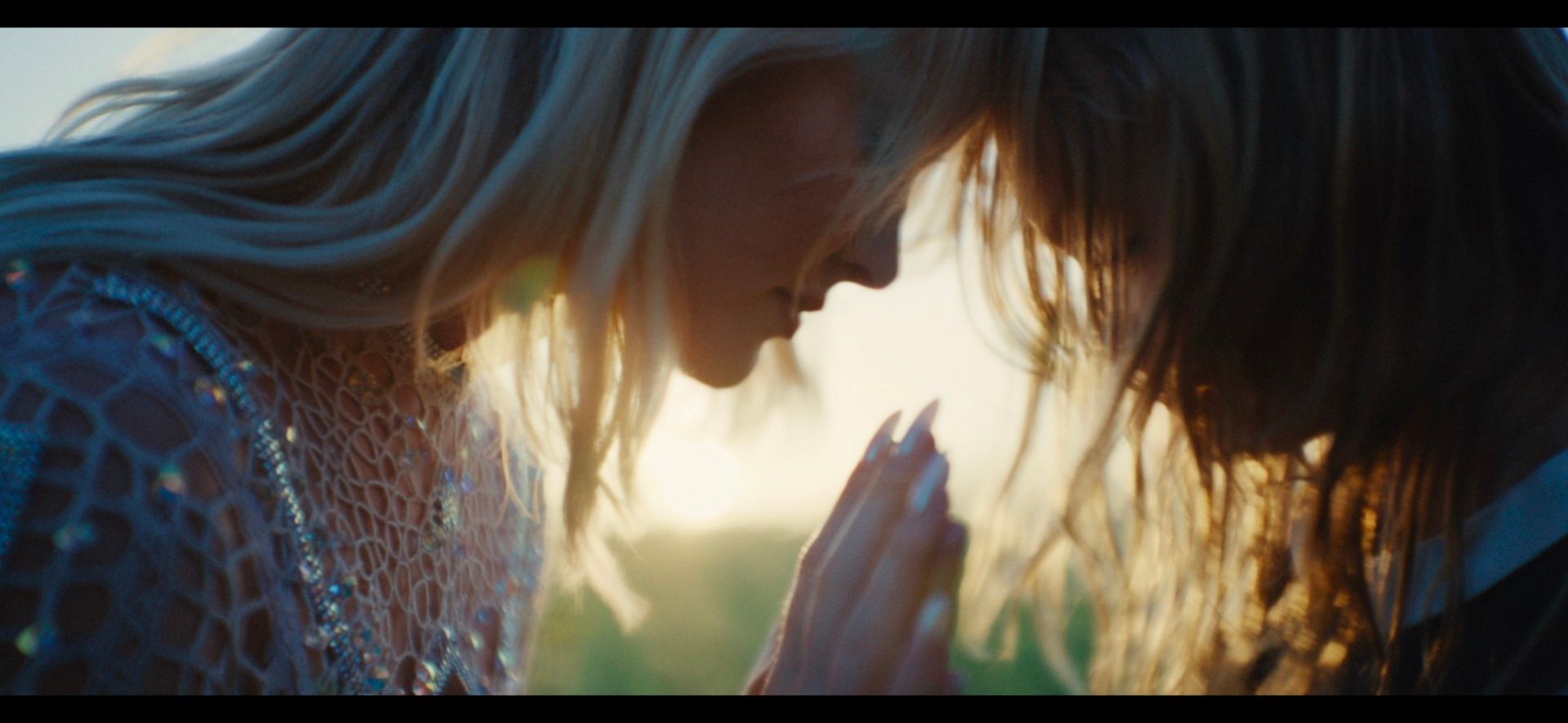 Two women in close embrace, hands clasped, bathed in warm golden hour light.