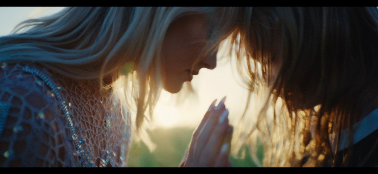 Two women in close embrace, hands clasped, bathed in warm golden hour light.