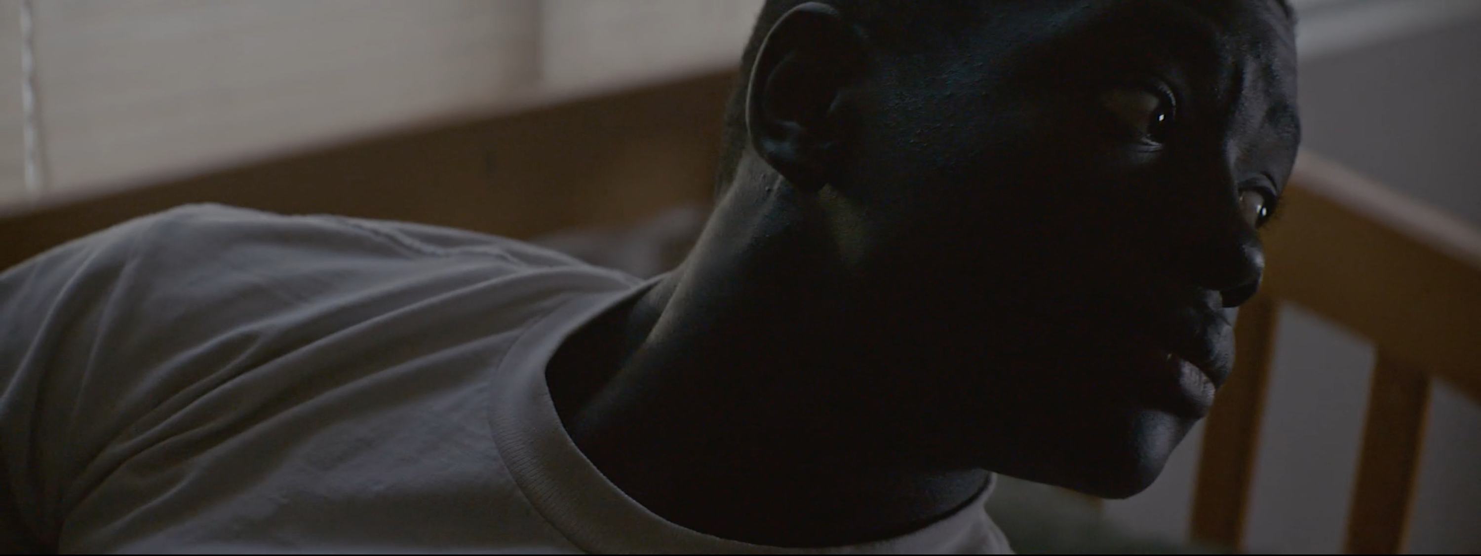 Close-up of a young Black man in shadow, looking off-camera with intense expression.