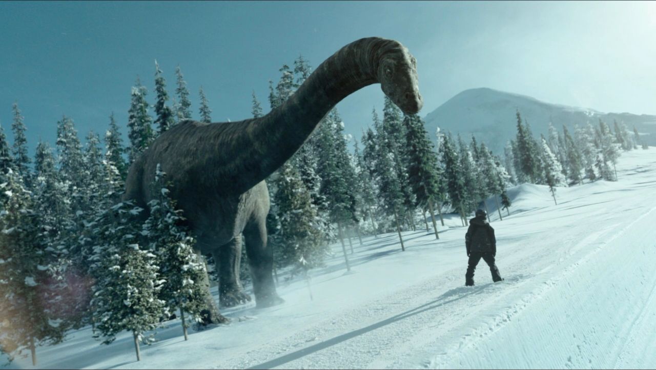 Shaun White stands on snowy slope facing a massive Brachiosaurus in winter forest