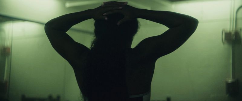 Silhouette of a woman with arms raised over head in a locker room setting.