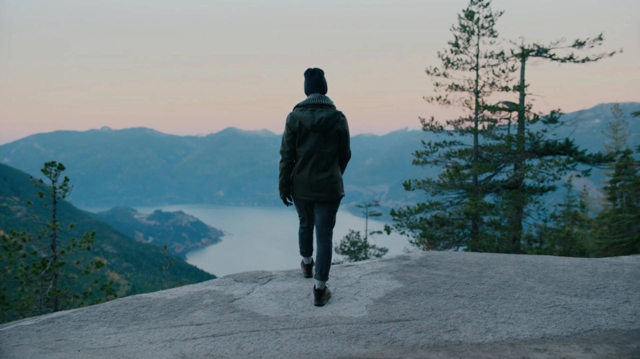 Person walking on rocky overlook toward mountain lake at dusk