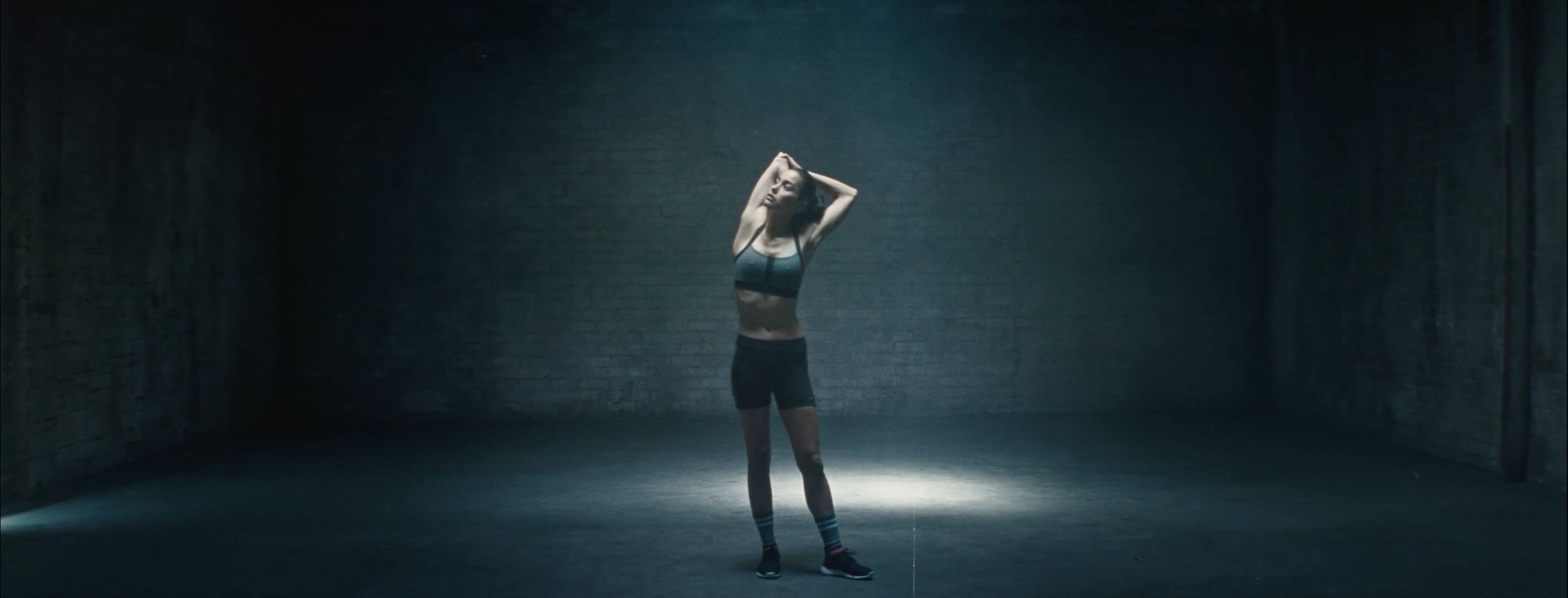 Woman in athletic wear stretching under dramatic spotlight in dim studio