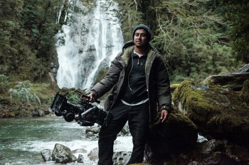 Cinematographer holding camera rig near waterfall in Patagonia wilderness.