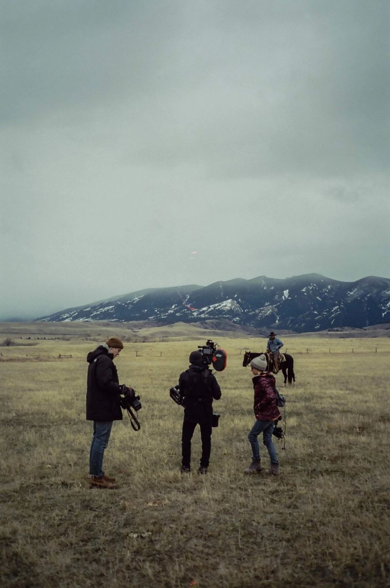 Film crew on open field with mountains in background, filming a rider on horseback