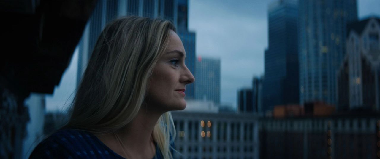 Blonde woman in profile looking out over a blurred city skyline.