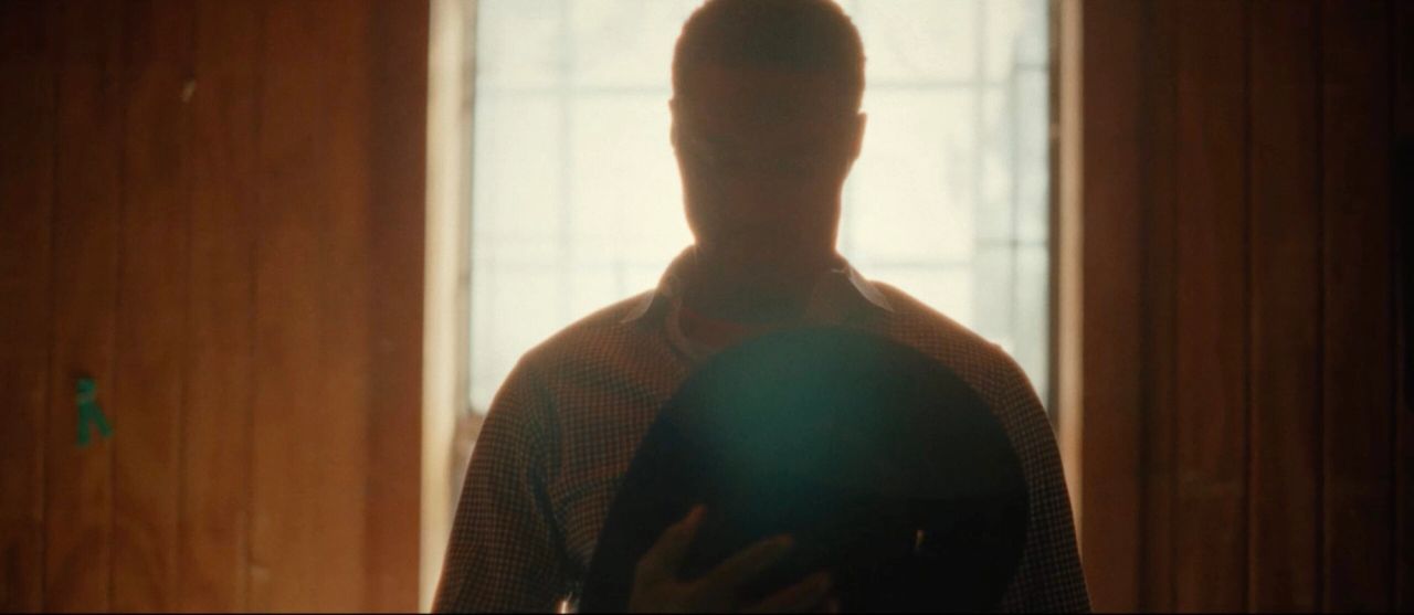 Silhouetted figure holding a cowboy hat in front of a bright window