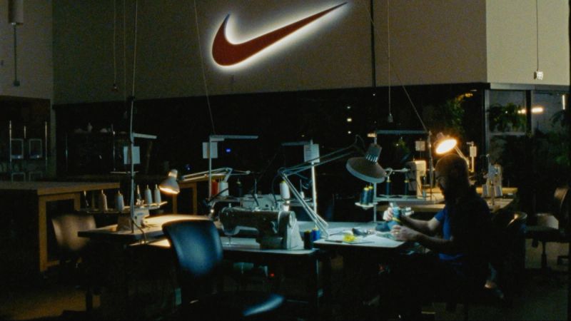 Seamstress working at sewing station under bright lamp in dimly lit Nike factory