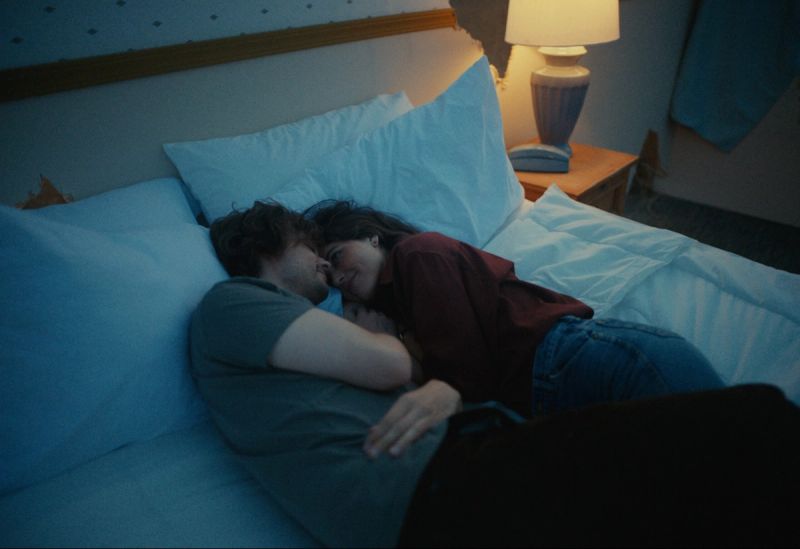 Couple embracing on a bed in dimly lit room with bedside lamp