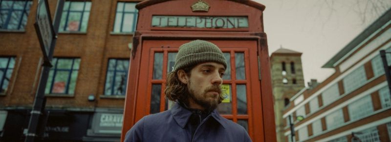 Cinematographer in beanie stands near red telephone booth during Nike Dear Nike location scouting.