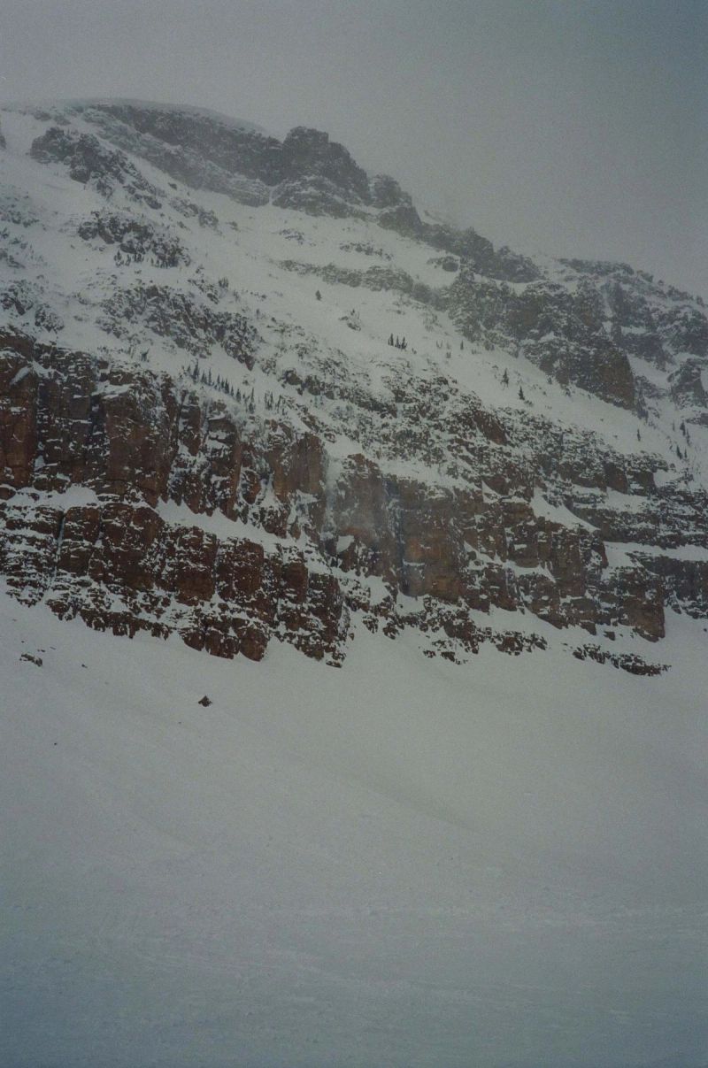 Snowy mountain slope with rocky outcrops under overcast, flat lighting conditions.