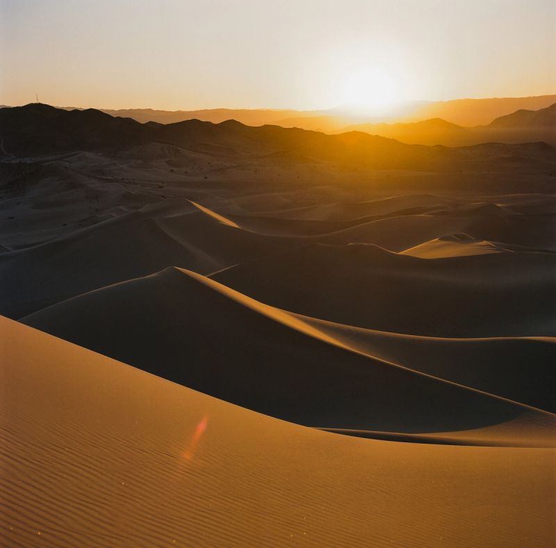 Golden hour desert dunes with distant mountains at sunset