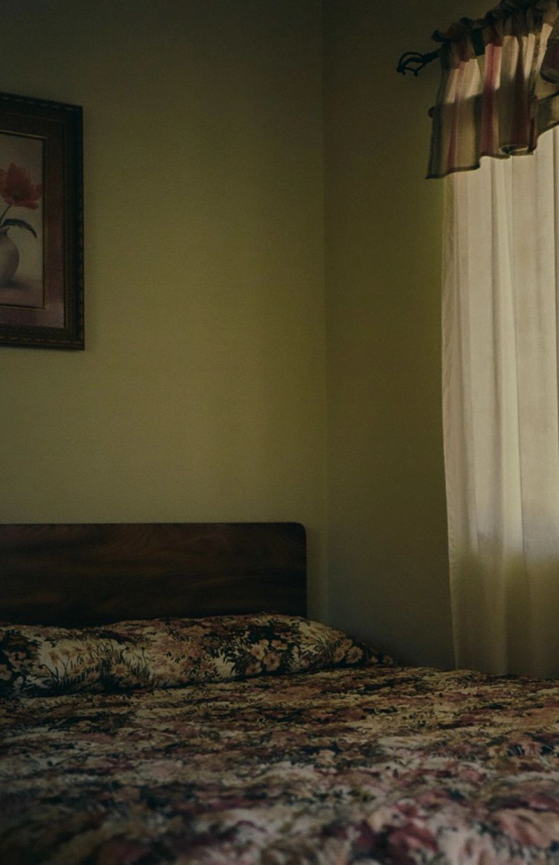 Bedroom scene with floral bedding, framed flower painting, and sheer curtains in soft natural light