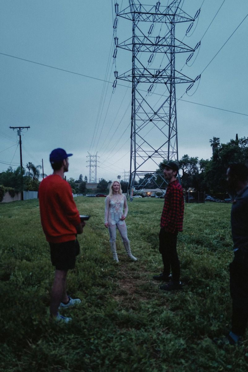 Zara Larsson stands in a field with three men near power lines at dusk