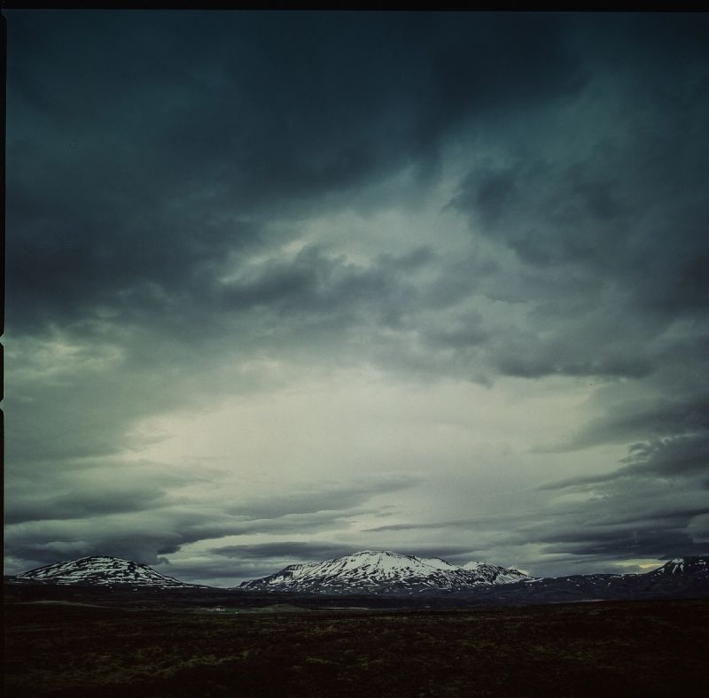 Dramatic cloudy sky over snow-capped mountains and dark tundra landscape in Iceland.