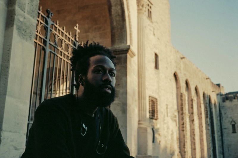 Cinematographer posing in front of historic stone arches and iron gate, captured on film in Paris France.