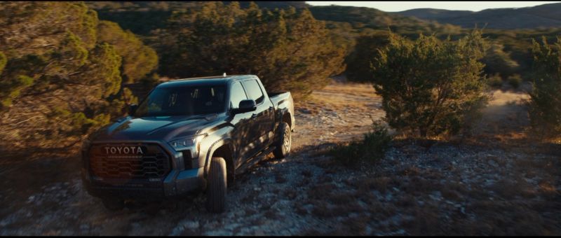 A dark Toyota Tundra pickup truck navigating a rocky off-road trail through scrub brush.