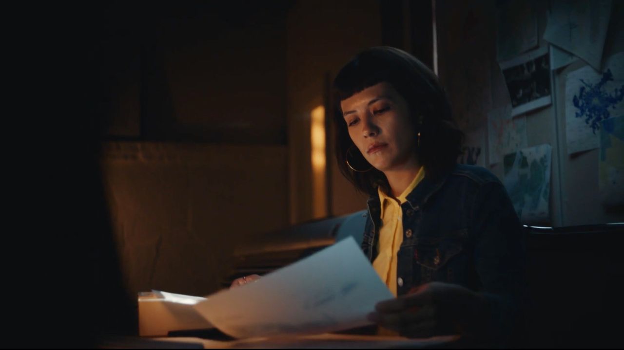 A woman reviews documents in a dimly lit office space with cinematic lighting.