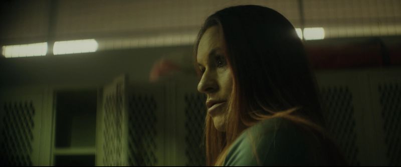 Profile of a female athlete in a dimly lit locker room with white lockers behind her.