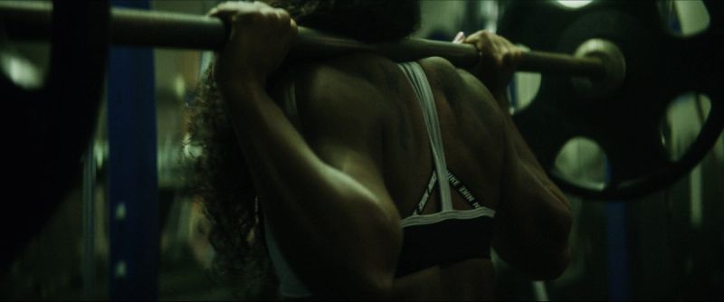 Woman lifting barbell on shoulders in gym for EastBay ConqHer Santia Deck project.
