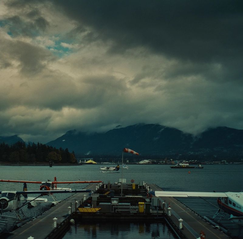 Seaplanes docked at a marina under stormy skies with mountains in the background
