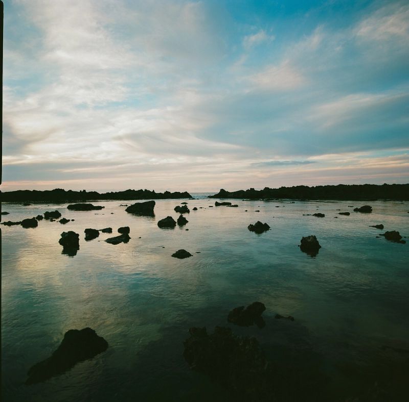 Calm ocean waters with scattered rocks under soft sky at sunset
