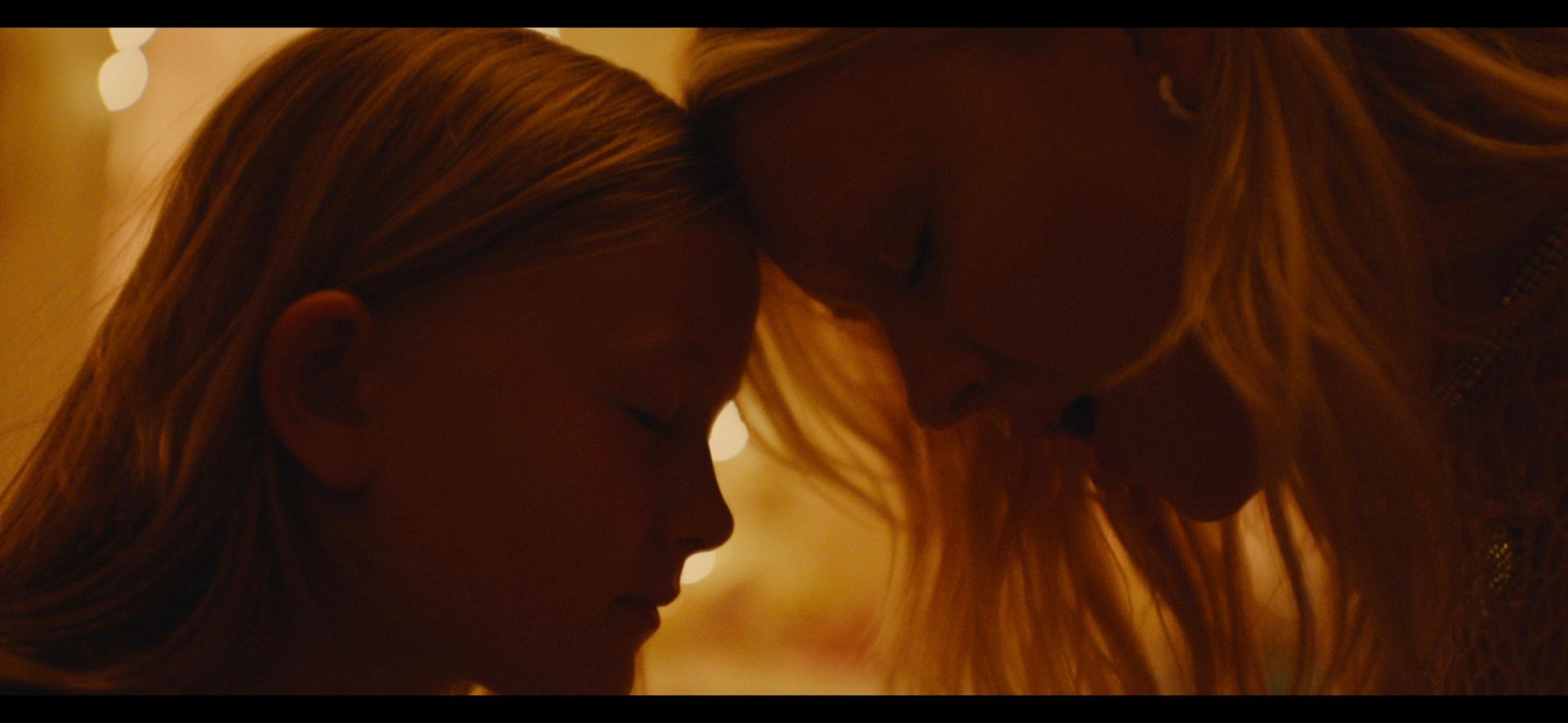 Zara Larsson and a young girl share an intimate, tender moment with foreheads touching in warm lighting.