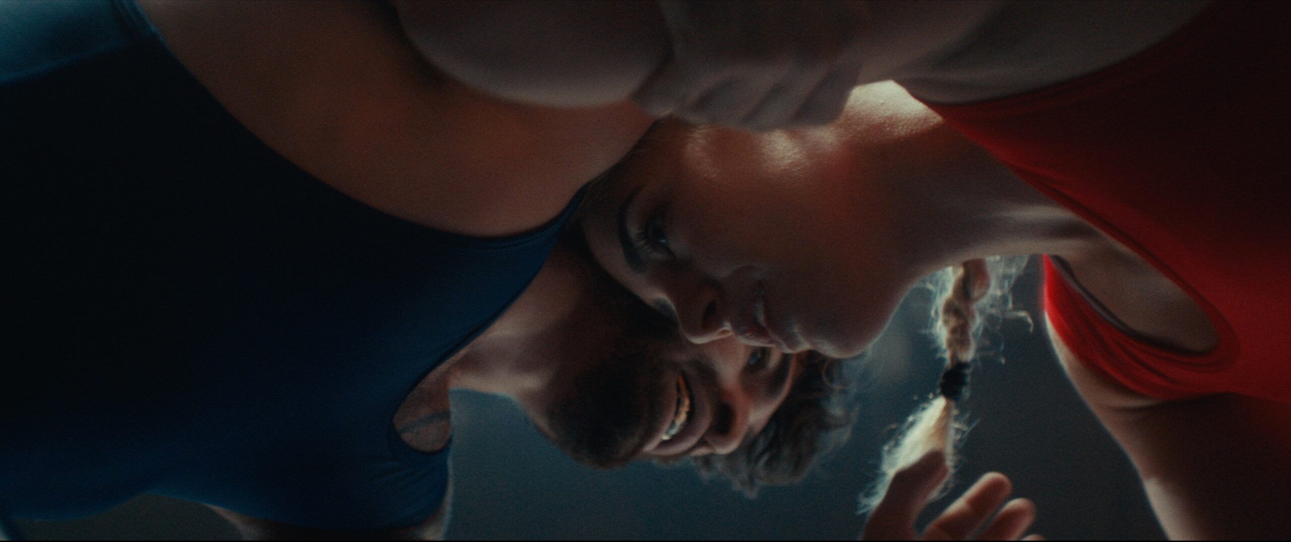 Close up low angle shot of two wrestlers in red and blue singlets grappling intensely.