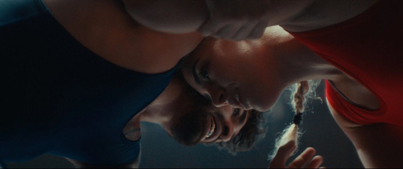 Close up low angle shot of two wrestlers in red and blue singlets grappling intensely.