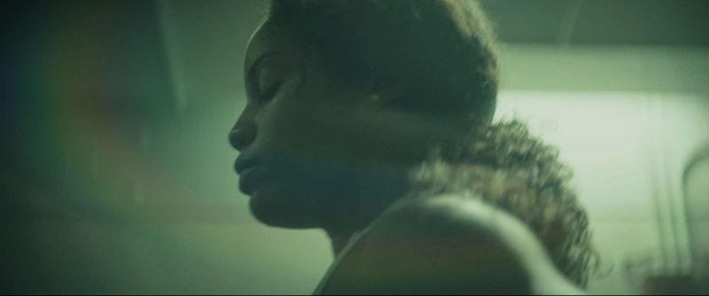 Profile portrait of a female football player with curly hair in a moody, green-lit gym setting.